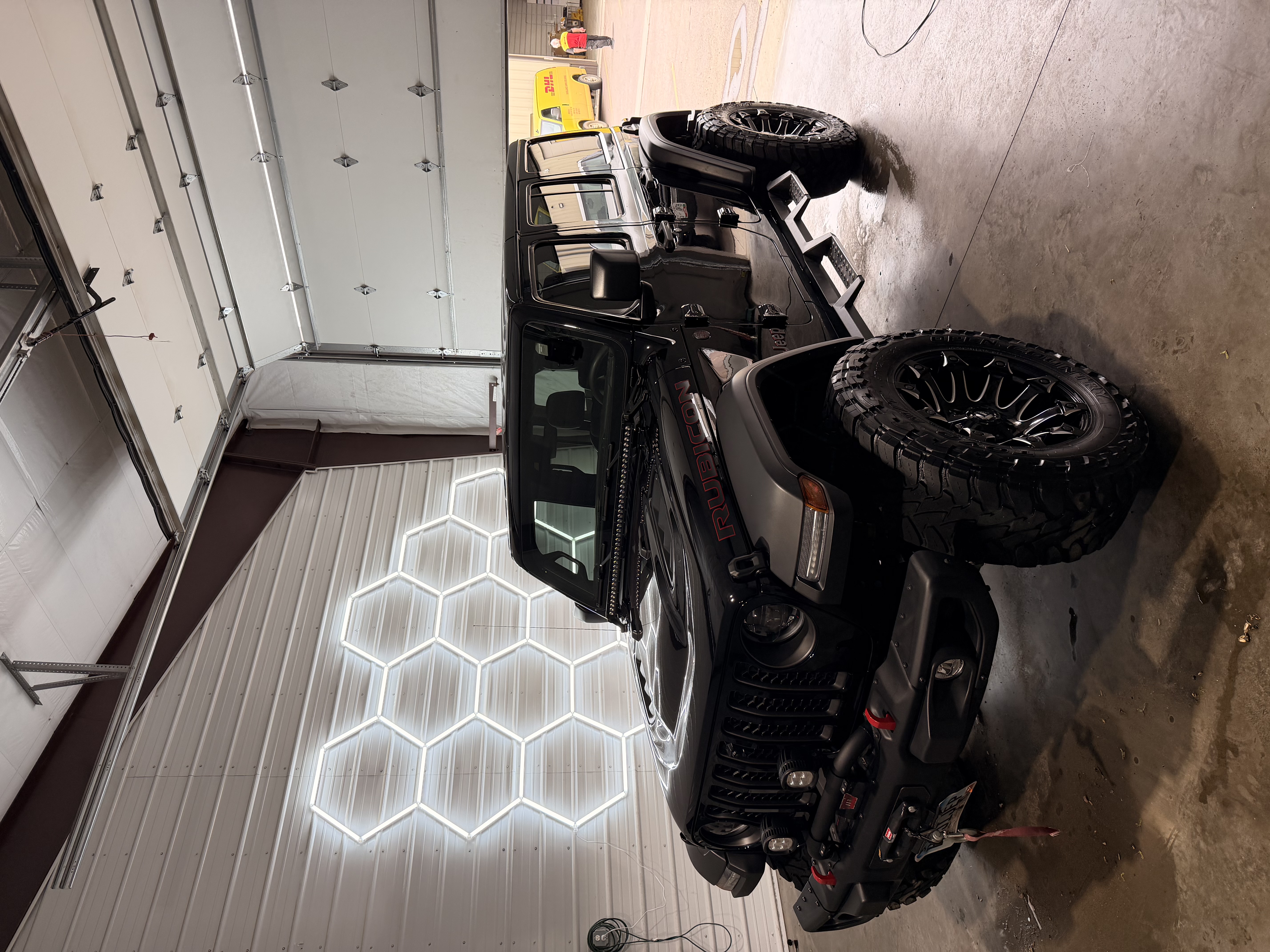 Glossy black Jeep Wrangler Rubicon under hexagon detailing lights, showing mirror-like paint reflections
